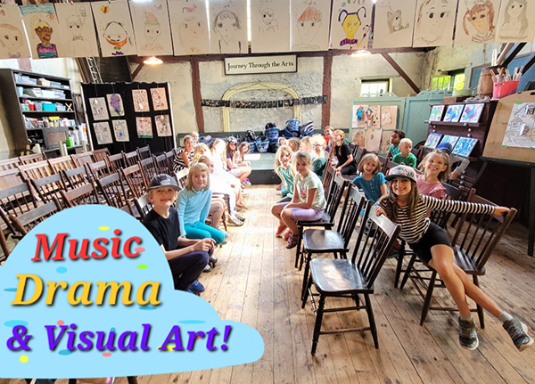 Children seated in rows facing a small stage in the rustic studio hall, their drawings displayed on the walls beneath a Journey Through the Arts banner.