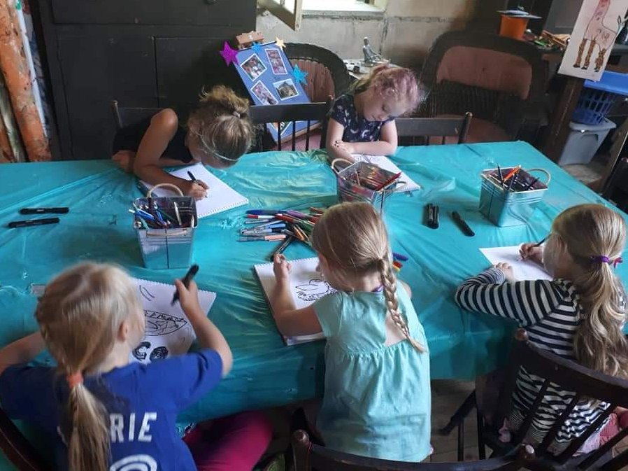 Young children gathered around a cloth-covered table, drawing with markers in the studio.