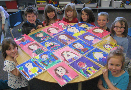 A group of young children around a table proudly displaying a grid of their painted self-portraits.