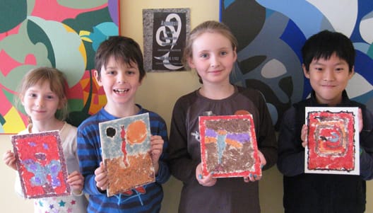 Four kids holding up their textured mixed-media paintings in front of a colourful mural.