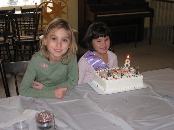 Two girls smiling beside a birthday cake with a number 8 candle.