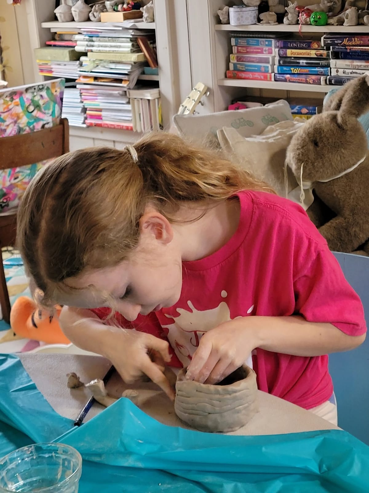 A girl building a clay coil pot at a table covered in a blue cloth.