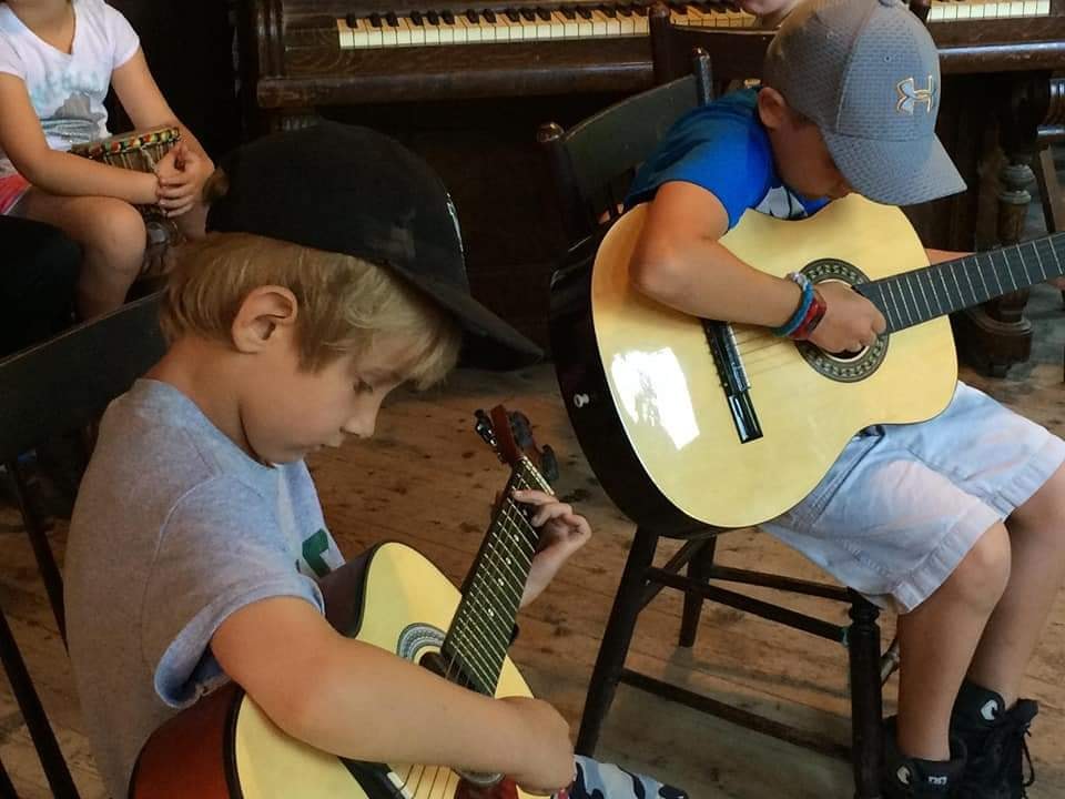 Two boys playing acoustic guitars, one in a black cap and one in a grey cap.
