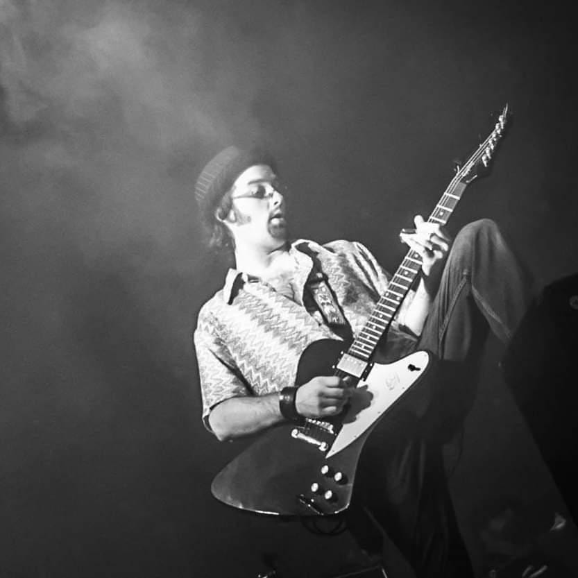 Mike Woods playing an electric guitar on a smoky stage, in black and white.